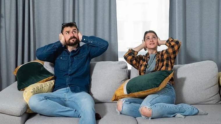 Sofrada oturan bir erkek ve kadın, gürültüden rahatsız olarak kulaklarını kapatıyor.