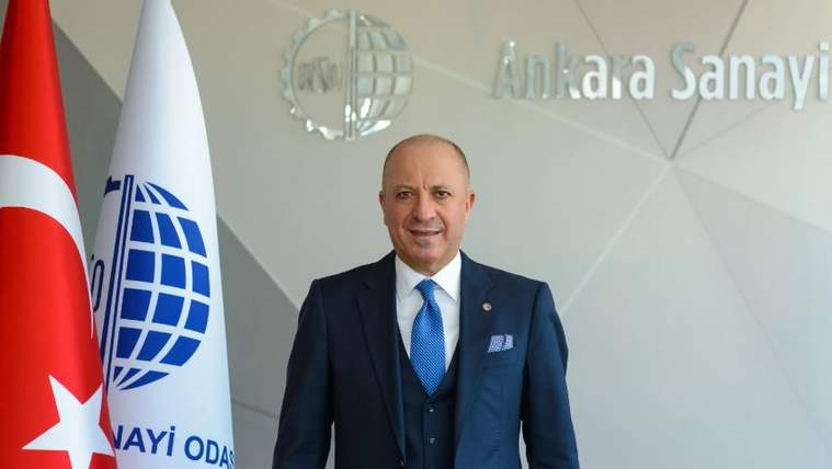 Ankara Sanayi Odası'nın logosunun önünde, takım elbise giymiş bir kişi gülümsüyor.