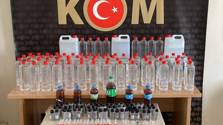 Üzerinde KOM yazılı bir arka planda, çeşitli boyutlarda şişeler ve alkol üretim kitleri sergileniyor.