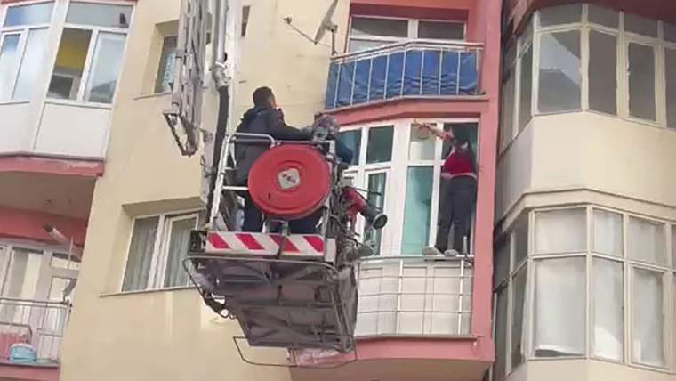 Bir itfaiye aracı, pencereye çıkan kadına yardım etmek için yukarıda duruyor.