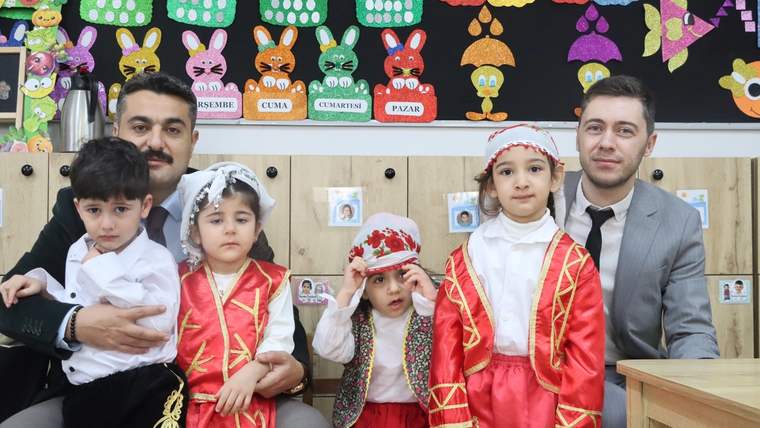Bir grup çocuk, geleneksel kıyafetler içinde, iki yetişkinle birlikte oturuyor.