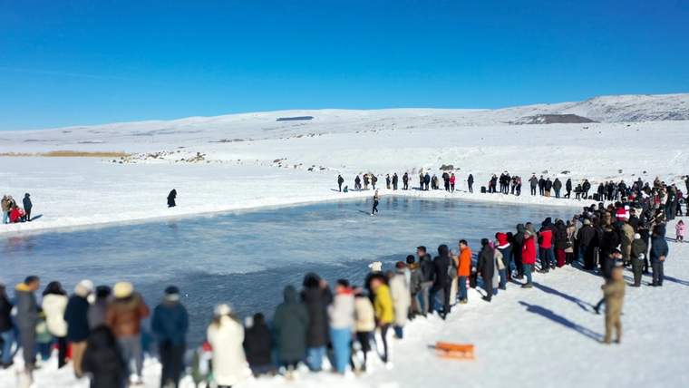 Karlarla kaplı göl çevresinde ve buzlu yüzey üzerinde sıralanan kalabalık insan topluluğu