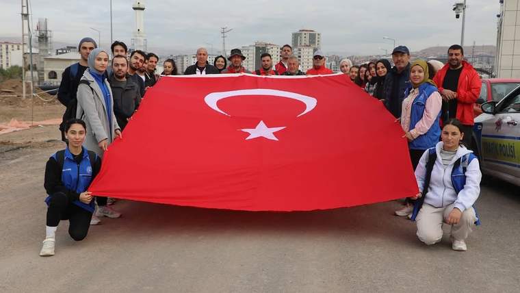 Bir grup insan, yol üzerinde büyük Türk bayrağını açarak kameraya doğru poz veriyor.