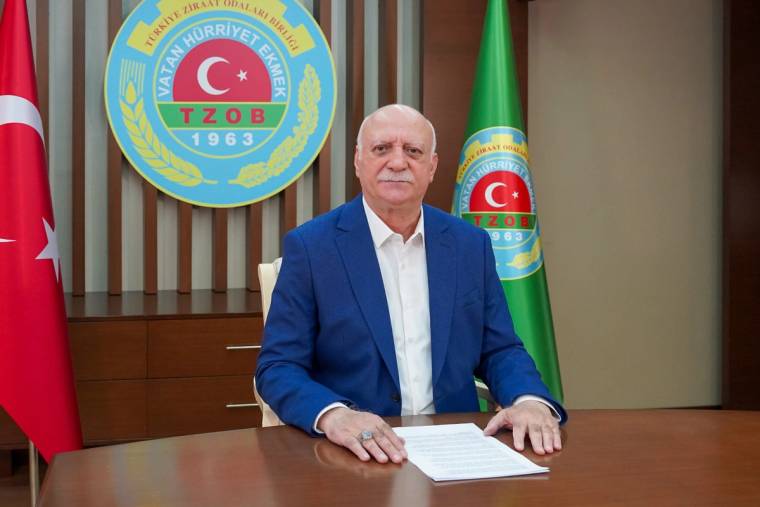 Masada oturan bir kişi, arkasında Türk bayrağı ve TZOB amblemleriyle kameraya bakıyor.