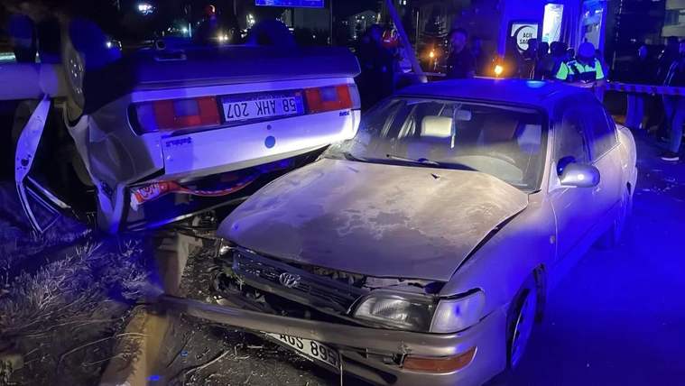 Gece vakti çarpışmış iki otomobil, mavi ışıklar altında hasarlı halde yol kenarında duruyor.