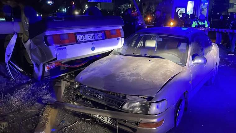 Gece vakti çarpışmış iki otomobil, mavi ışıklar altında hasarlı halde yol kenarında duruyor.