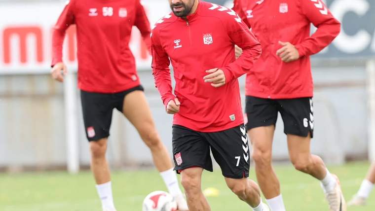 Kırmızı forma giymiş futbolcular antrenman yapıyor, biri önde koşuyor.