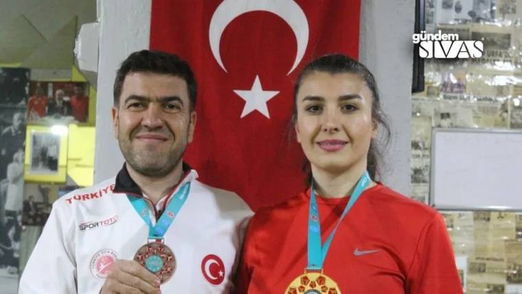 Türk bayrağı önünde duran bir erkek ve kadın, boyunlarında madalyalarla kameraya bakıyor.