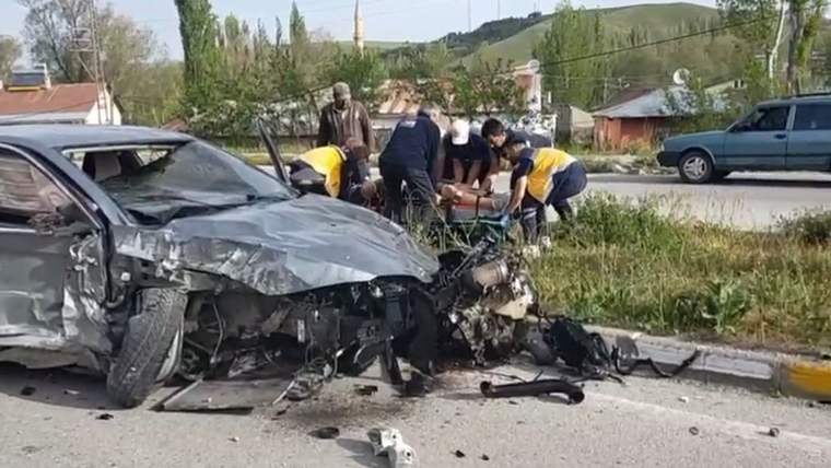 Ön kısmı ağır hasar almış otomobilin yanında, yol kenarında sedyeye müdahale eden kişiler görülüyor.