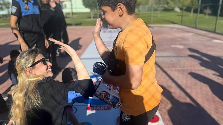 Bir çocuk, etkinlikte bir yetişkinle el şakası yapıyor. Arka planda başka katılımcılar var.