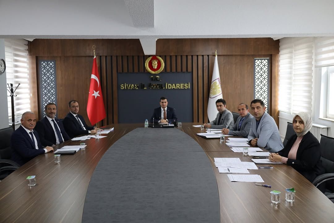 Sivas İl Özel İdaresi yazılı salonda, uzun masa çevresinde toplantı yapan dokuz kişi ve Türk bayrağı görülüyor.