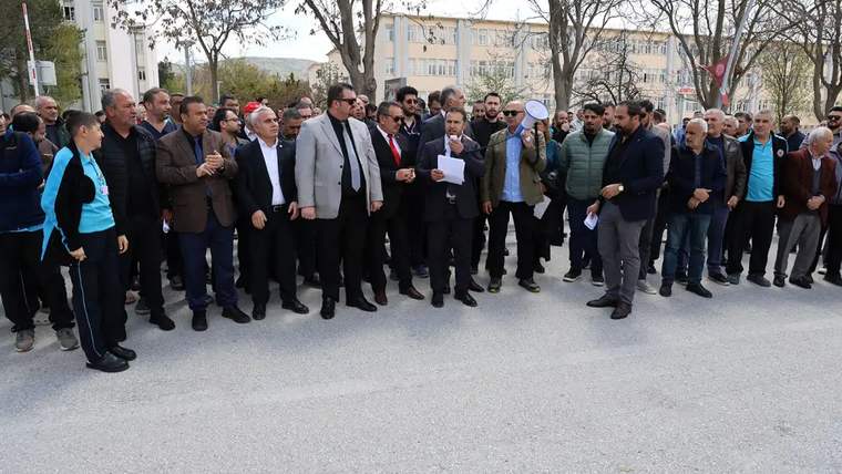 Bir grup insan, açık alanda toplanmış, bir kişi elinde kağıt tutarak konuşuyor.