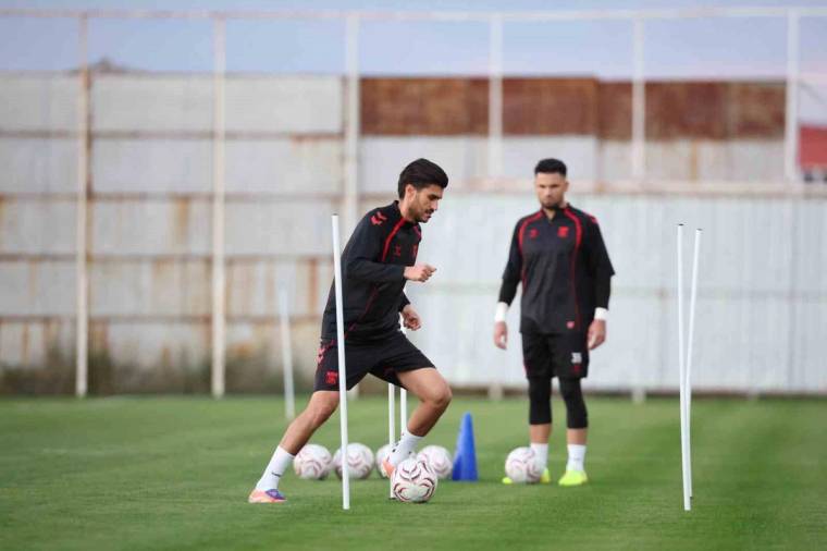 Çim sahada iki futbolcu antrenman yapıyor; öndeki top sürerken çevresinde slalom direkleri ve koniler bulunuyor.
