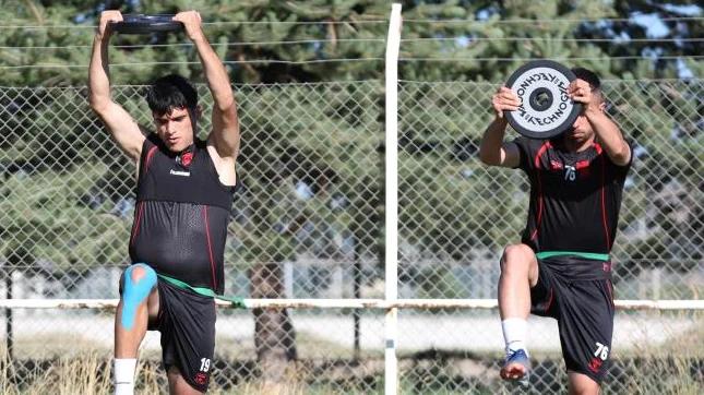 İki futbolcu, antrenman sahasında ağırlıklarla çalışıyor.