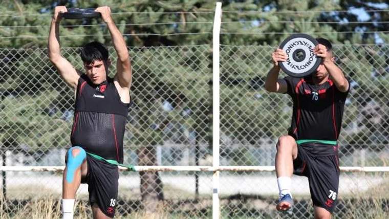 İki futbolcu, antrenman sahasında ağırlıklarla çalışıyor.
