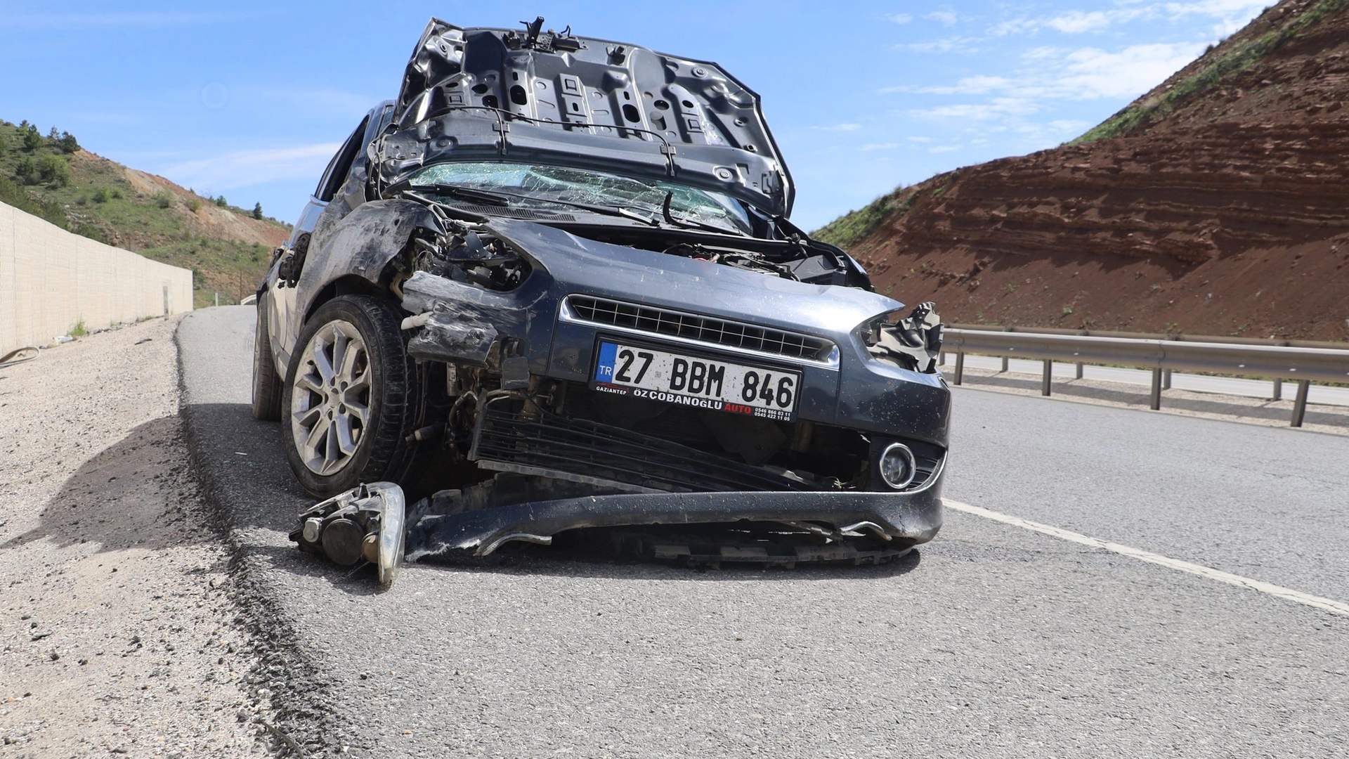 Ön kısmı ağır hasar gören otomobil, bölünmüş yolda istinat duvarı ve bariyerler arasında duruyor.