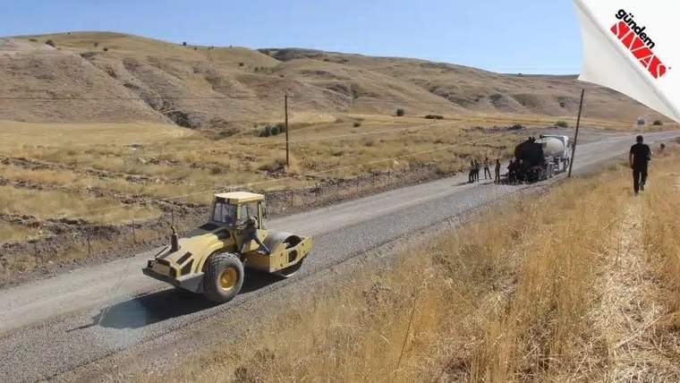 Yolda çalışan bir silindir, arka planda işçiler ve toprak alanlar görünmekte.