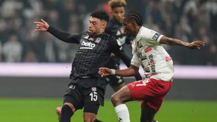 Siyah formalı futbolcu ile beyaz-kırmızı formalı futbolcu, saha içinde top için mücadele ediyor.