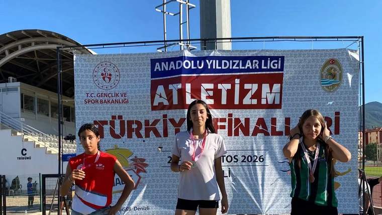 Üç genç atlet, üzerinde “1”, “2” ve “3” yazan podyumda, atletizm finalleri pankartı önünde duruyor.