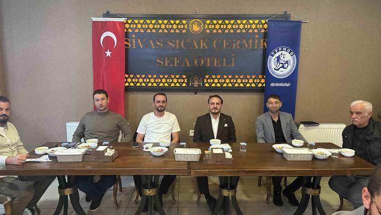 Bir otelde masada oturan kişiler, arkalarında Türk bayrağı ve üzerinde Sivas Sıcak Çermik Sefa Oteli yazılı pankartla görülüyor.