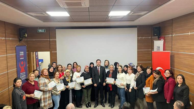 Toplantı salonunda bir erkek ve çok sayıda kadın, ellerindeki sertifikalarla birlikte kameraya bakıyor.