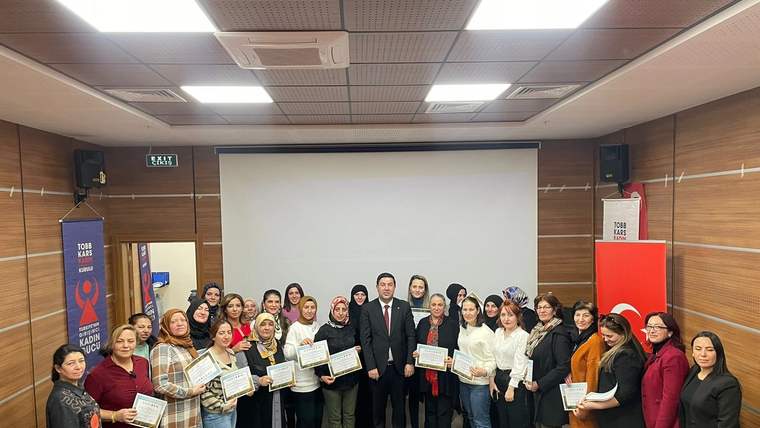 Toplantı salonunda bir grup kadın ve iki erkek, ellerindeki sertifikalarla birlikte objektife bakıyor.