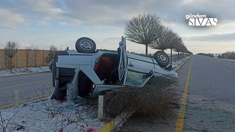 Yolda ters dönmüş bir otomobil, yanındaki çalılıkların üzerine devrilmiş durumda.