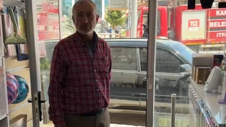 Bir dükkanda duran bir kişi, arka planda itfaiye aracı görünmekte.
