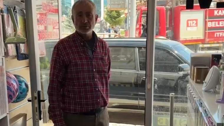 Bir dükkanda duran bir kişi, arka planda itfaiye aracı görünmekte.