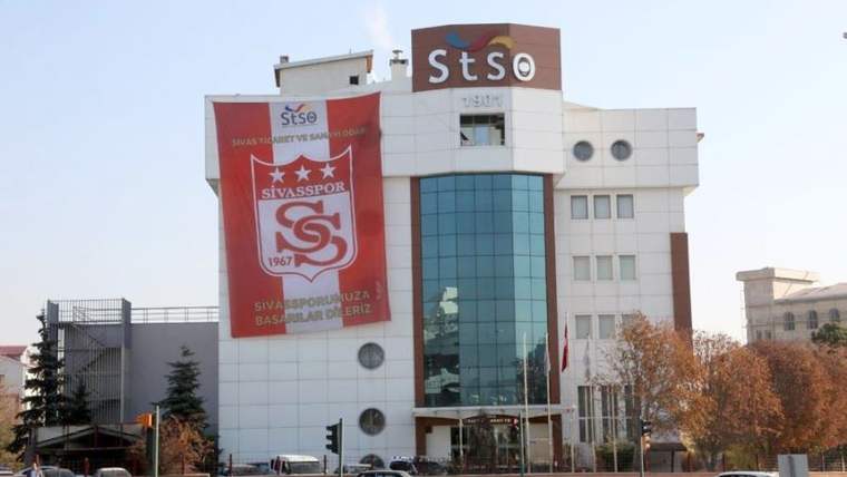 Üzerinde STSO ve Sivasspor yazıları bulunan, cam cepheli bir bina yol kenarında görülüyor.