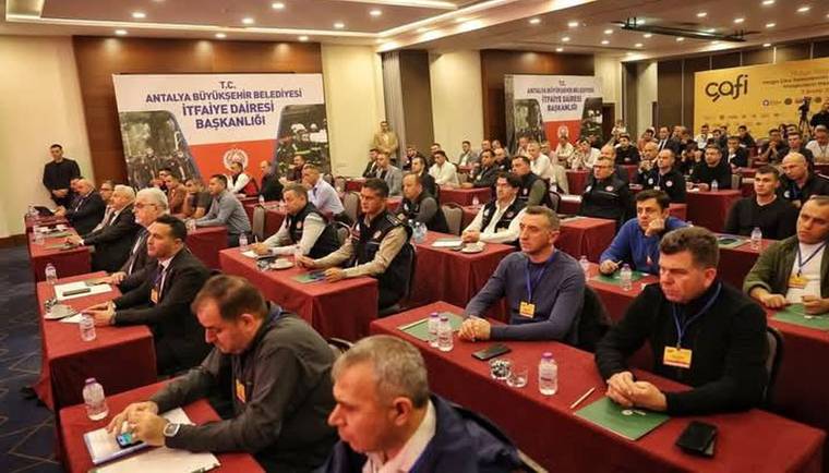 Toplantı salonunda sıralar halinde oturan kalabalık, önlerinde su şişeleri ve not defterleriyle görülüyor.
