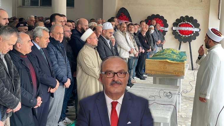 Cenaze töreninde, ön planda bir adam ve arka planda kalabalık bir grup yer alıyor.
