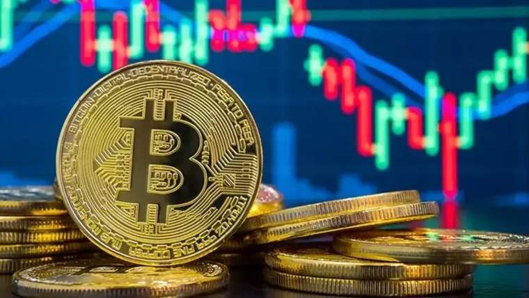 Ön planda Bitcoin simgeli altın renkli madeni para, arkasında düşüş eğilimli grafik ve madeni paralar görülüyor.