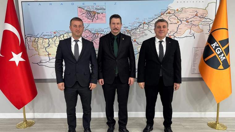 Harita önünde yan yana duran üç kişi, iki yanında Türk bayrağı ve Karayolları Genel Müdürlüğü bayrağıyla görülüyor.