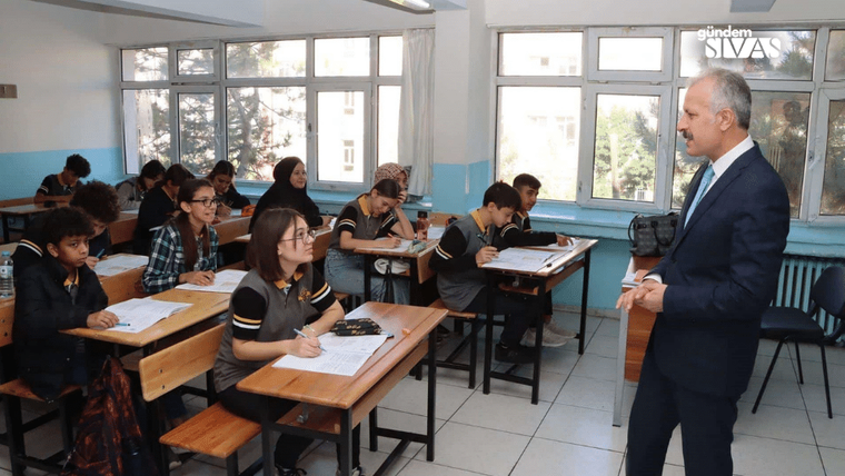 Sınıfta oturan öğrenciler, öğretmene dikkatle bakarak sınav yapıyorlar.