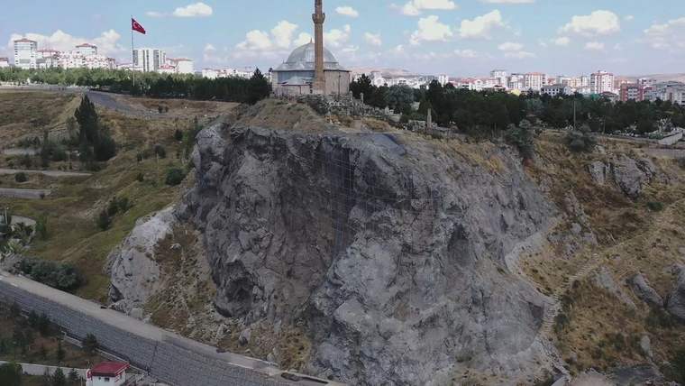 Kayalık bir tepenin üstünde kubbeli ve minareli yapı, çevresinde istinat duvarı ve şehir yerleşimi görülüyor.