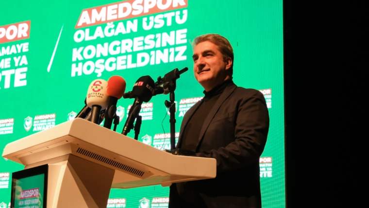 Bir kişi, Amédspor'un olağanüstü kongresinde konuşma yapıyor, arka planda yeşil bir pankart var.