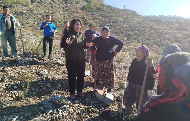 Kayalık yamaçta kürek taşıyan kadınlar ve çevrelerinde duran kişiler görülüyor.