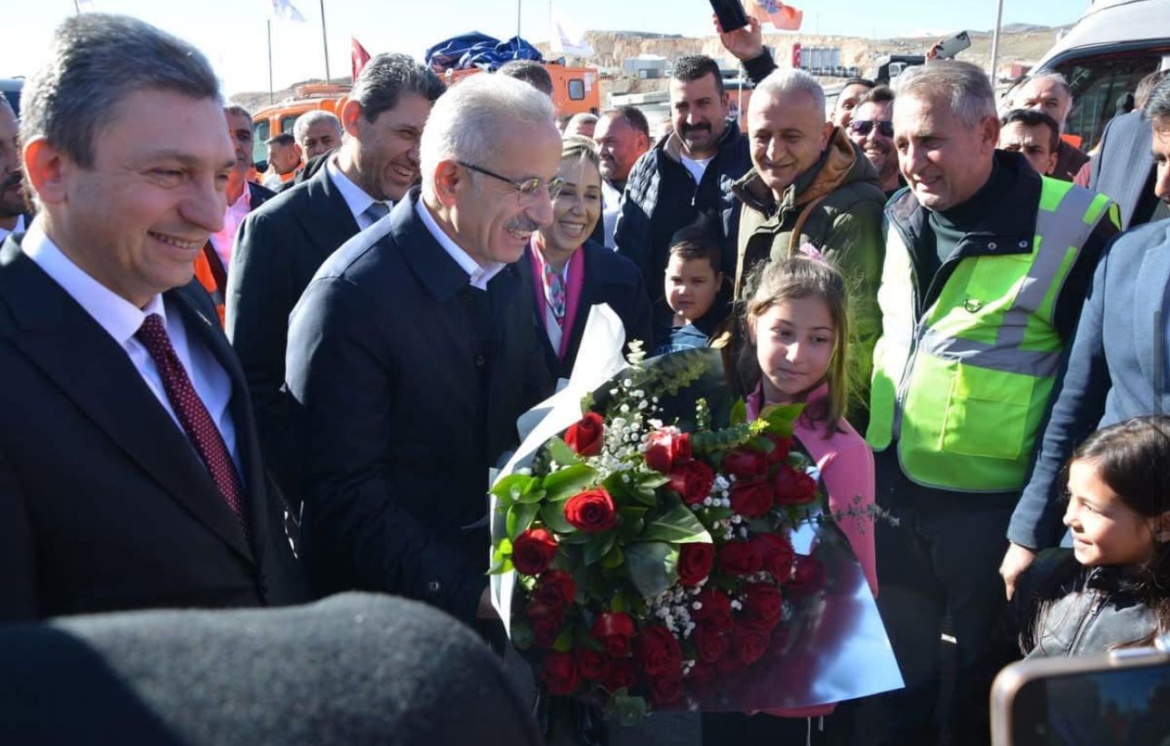 Kalabalık arasında bir kız çocuğu, elindeki çiçek buketini takım elbiseli bir erkeğe uzatıyor.