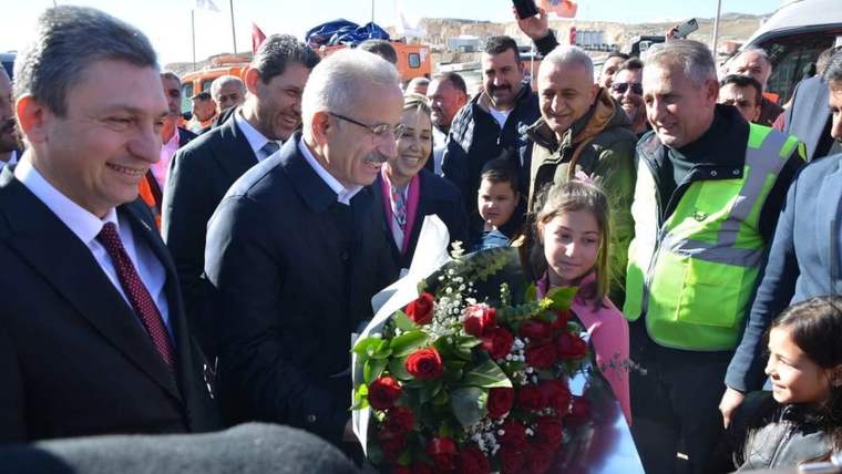 Kalabalık arasında bir kız çocuğu, elindeki çiçek buketini takım elbiseli bir erkeğe uzatıyor.