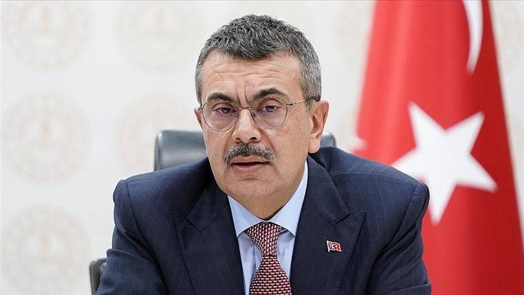 Kırmızı kravat takan bir kişi, masada oturarak konuşuyor.