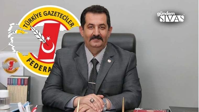 Bir masa etrafında oturan, takım elbise giymiş bir kişi, arkasında Türkiye Gazeteciler Federasyonu logosu var.