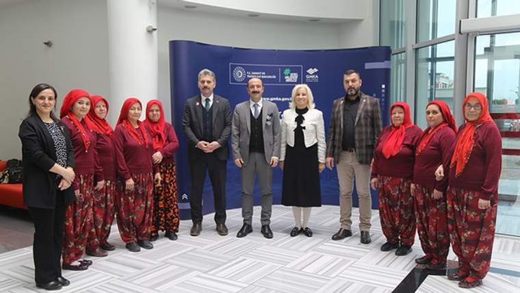 Bir etkinlik alanında, aralarında başörtülü kadınların ve takım elbiseli kişilerin bulunduğu grup yan yana duruyor.