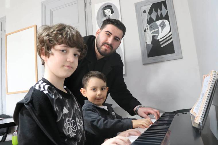 Piyano çalan iki çocuk ve yanında bir genç, sanat odasında birlikte çalışıyorlar.
