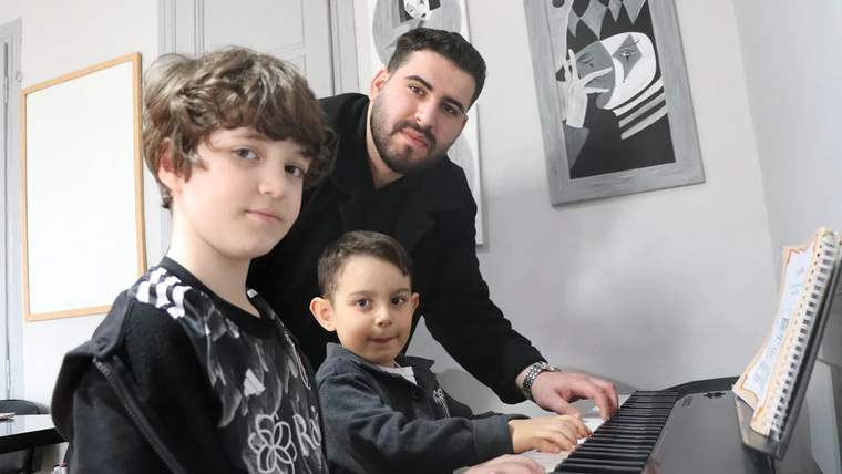 Piyano çalan iki çocuk ve yanında bir genç, sanat odasında birlikte çalışıyorlar.