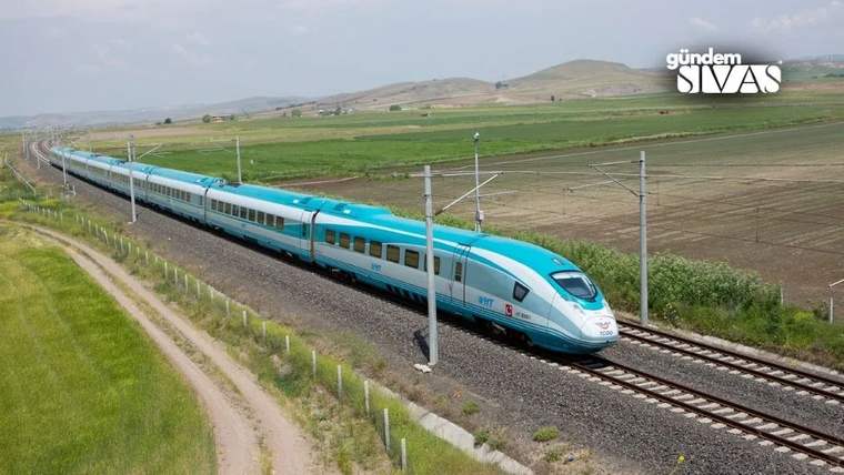 Mavi-beyaz renkte yüksek hızlı tren, tarım arazileri arasında raylar üzerinde ilerliyor.