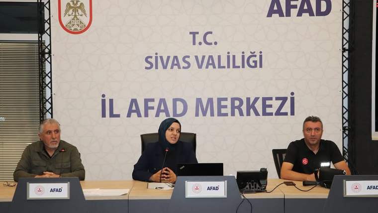 AFAD logolu panonun önünde, masada oturan üç kişi ve önlerinde isimlikler görülüyor.