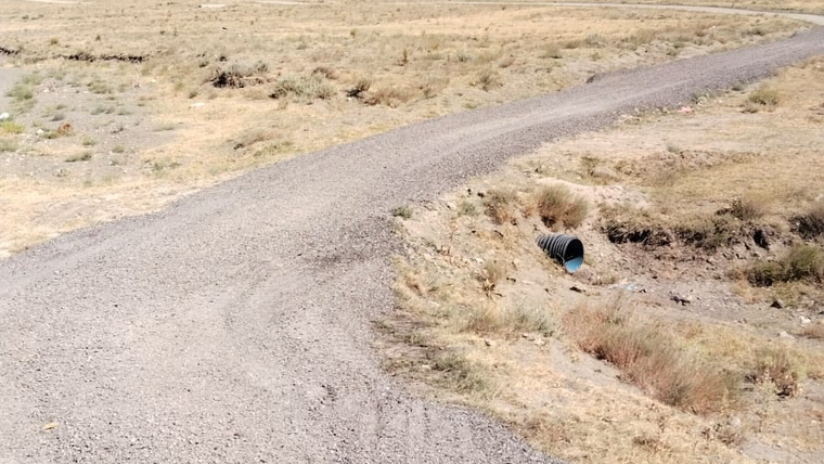 Kuru bir arazide, çöp toplama merkezi yoluna giden toprak yol ve yanındaki drenaj borusu görünmekte.