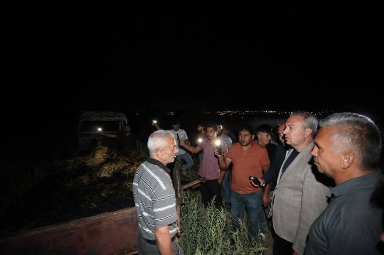 Gece karanlığında, bir grup insan yanmış bitki örtüsü ve enkazın yanında konuşuyor.