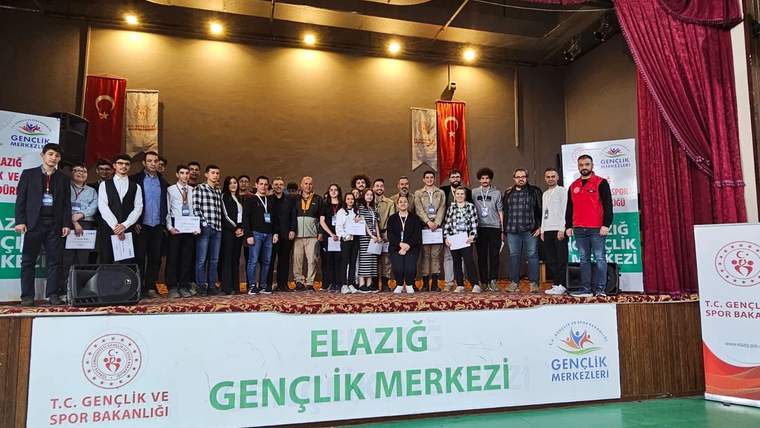 Sahnede madalya ve belgeler taşıyan kalabalık, Elazığ Gençlik Merkezi yazılı pankartın önünde duruyor.